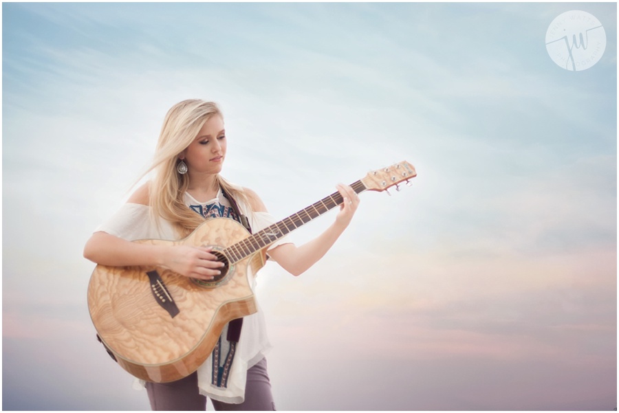 High school senior girl plays acoustic guitar at sunset by the lake